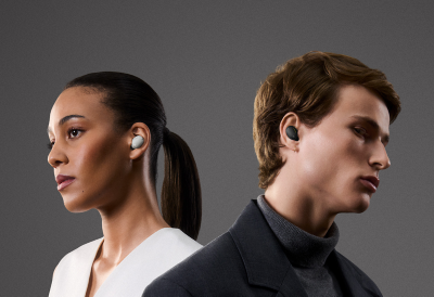 Záběr z boku na mladou ženu v bílém s bílým sluchátkem v uchu. Na druhou stanu otočený muž oblečený v černém a šedém má v druhém uchu černé sluchátko.
