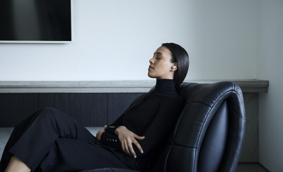 Một cô gái trẻ đang ngồi trên ghế da với đôi mắt nhắm lại, trên tai là tai nghe màu trắng.