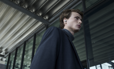 한 젊은 남성이 화이트 이어버드를 착용하고 창문이 여러 개 있는 장소를 지나갑니다.