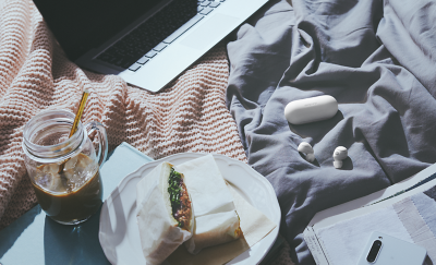 白色 WF-C700N 耳塞式耳機和充電盒擺放在床上，旁邊是筆記型電腦與咖啡