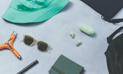 Image of sage green WF-C700N headphones and case surrounded by various items such as a hat, notebook, bag and sunglasses