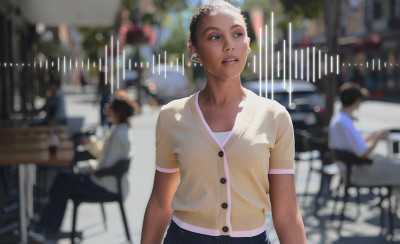 Một người đang đi qua trên đường phố nhộn nhịp và đeo tai nghe LinkBuds Clip, với ảnh đồ họa sóng âm để minh họa chế độ Voice Boost (Tăng cường giọng nói)