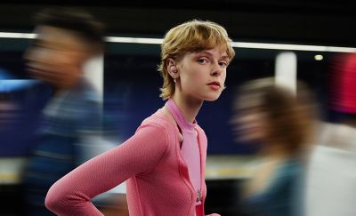 A woman dressed in pink is seen in a busy public area wearing the new WF-1000XM5 Noise Cancelling Headphones