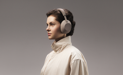 Woman in a high-collar beige jacket wearing Sony WH-1000XM6 headphones, side profile view, neutral background.