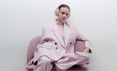 분홍색 오버사이즈 정장에 샌드 핑크 헤드폰을 착용하고 편안한 의자에 앉아 있는 젊은 여성.