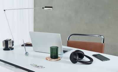 A pair of black 1000X THE COLLEXION headphones on a white table near a phone, a laptop, and a glass