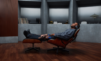 A person wearing some 1000X THE COLLEXION headphones reclined on a brown chair in a room with grey walls