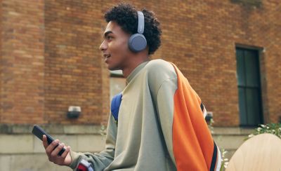 Image d'un homme assis sur un mur portant un casque Sony WH-CH520 et tenant un téléphone portable avec un skateboard au premier plan