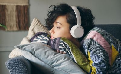Image of a woman lying on a grey sofa wearing a pair of white Sony WH-CH520 headphones