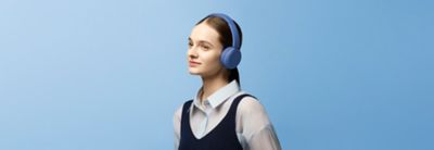 Mlada manekenka nosi kobaltne slušalice Sony WH-CH530 naspram jednobojne plave pozadine