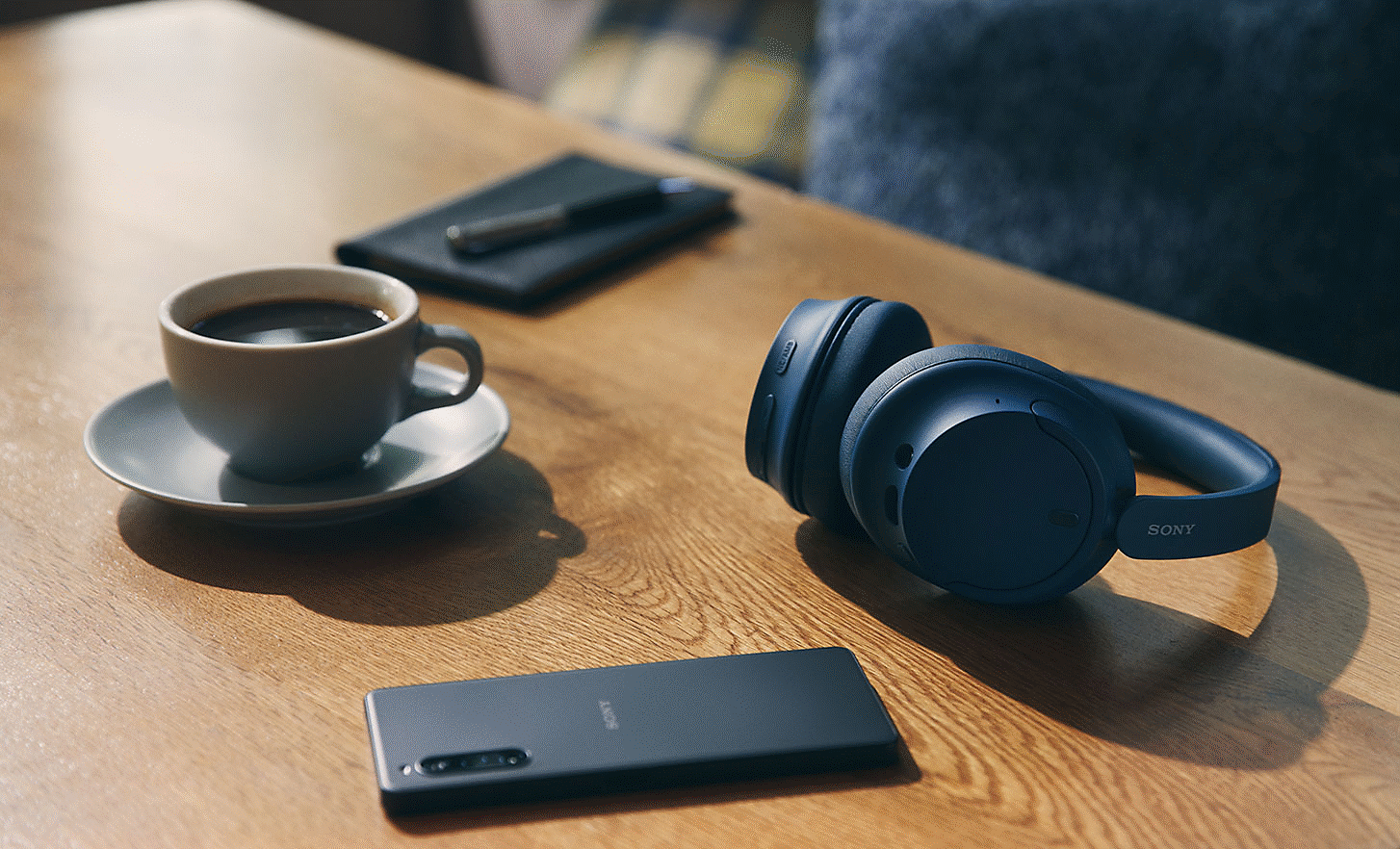 Image of a black pair of Sony WH-CH720 headphones sitting on a desk with an Xperia mobile phone
