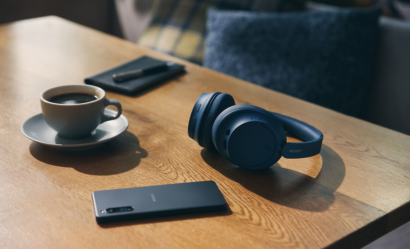 Imagine cu o pereche de căști Sony WH-CH720 negre pe birou, alături de un telefon mobil Xperia