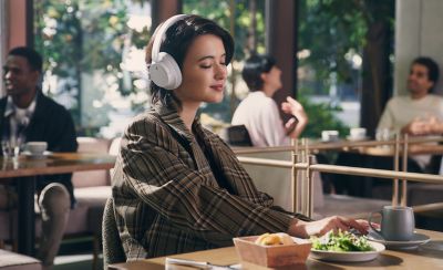 Image of a woman in a restaurant listening to music on a white pair of Sony WH-CH720 headphones