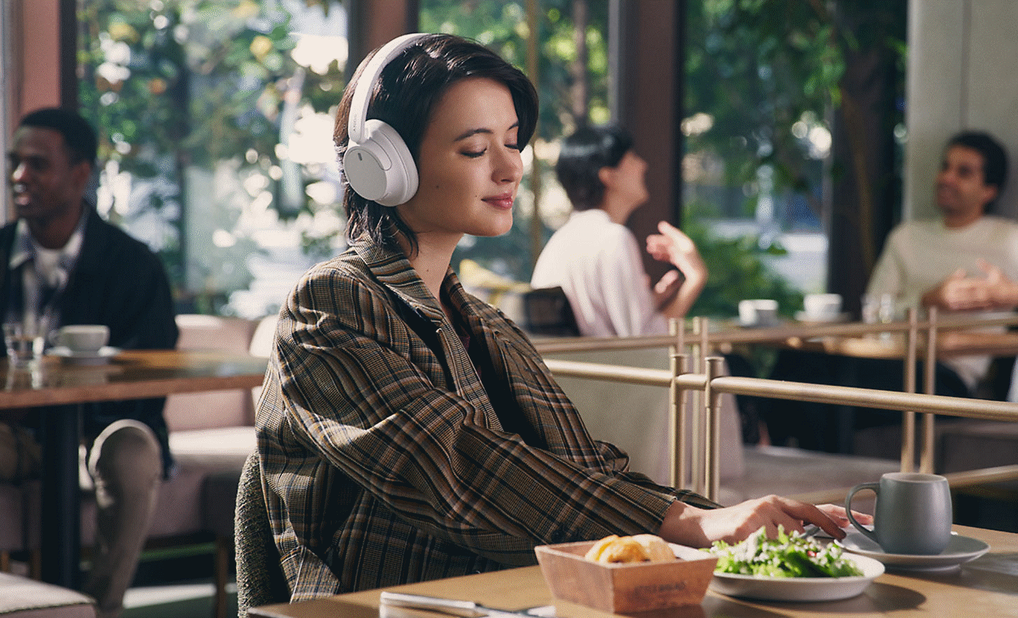 一位女性在餐廳裡用一副白色 Sony WH-CH720 耳機聽音樂的影像