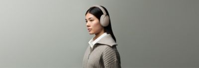 Žena nosi bež slušalice Sony WH-CH730N naspram obične sive pozadine
