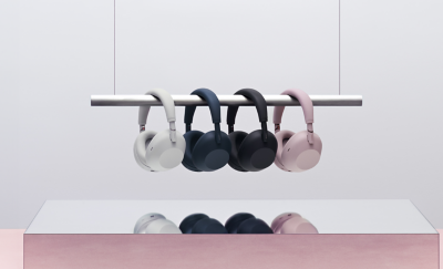 핑크색 받침대가 있는 거울로 된 표면 위로 디스플레이용 레일에 화이트, 네이비, 블랙, 샌드 핑크 색상의 헤드폰 네 개가 걸려 있습니다.