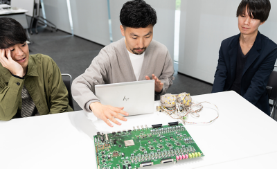 WH-1000XM6 사운드 튜닝 및 테스트에 사용되는 오디오 회로기판에 관해 논의 중인 개발자의 이미지