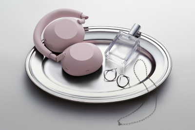 코너에 놓인 핑크색 케이스에 기대어 놓은 핑크 헤드폰. 금속 느낌의 양쪽 벽면에 두 개의 모습이 흐리게 비칩니다. 