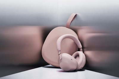 코너에 놓인 핑크색 케이스에 기대어 놓은 핑크 헤드폰. 금속 느낌의 양쪽 벽면에 두 개의 모습이 흐리게 비칩니다. 