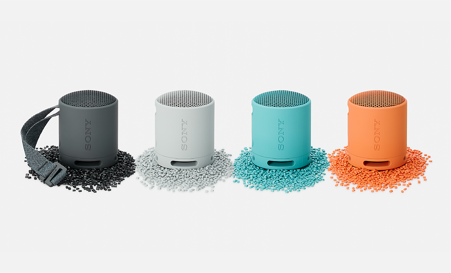 Afbeelding van de zwarte, witte, blauwe en oranje SRS-XB100-speakers die op plastic korrels in dezelfde kleur staan.