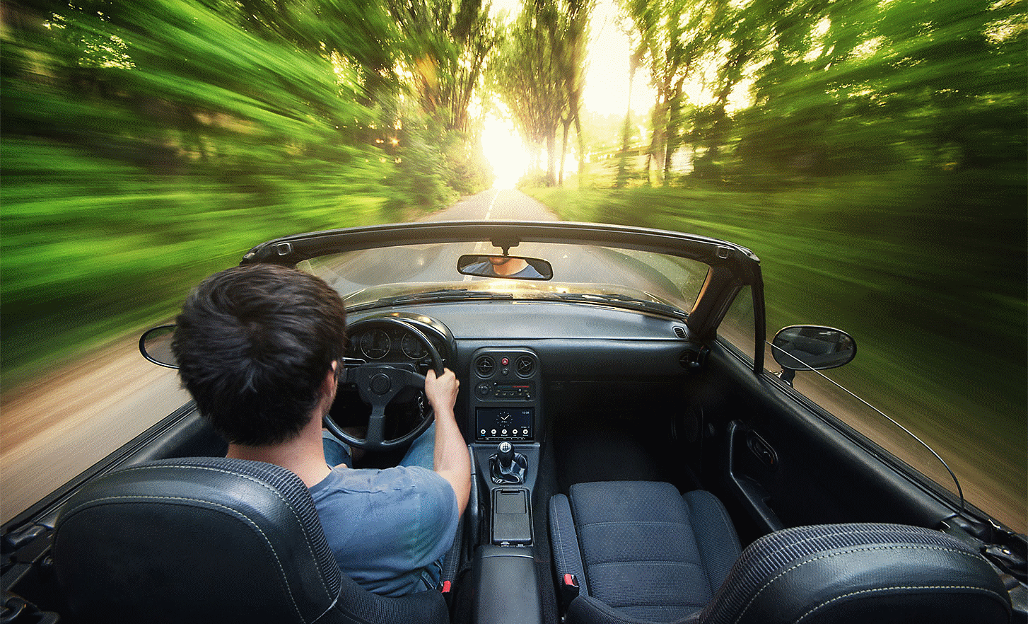 Snímek osoby řídící kabriolet jedoucí vysokou rychlostí po silnici lemované stromy. Přehrávač XAV-AX4050 je součástí palubní desky