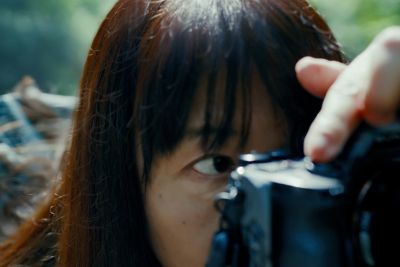 Primer plano de un fotógrafo mirando por el visor electrónico de una cámara mientras toma una foto en el exterior.