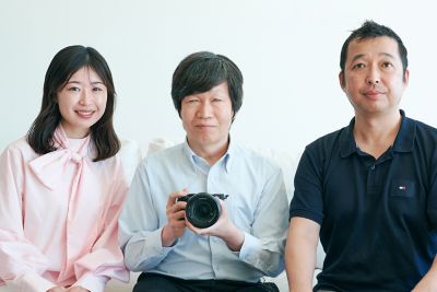 Tres personas sentadas juntas, la persona en el centro sostiene una cámara.