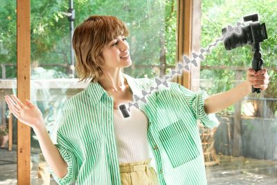 Hình ảnh sử dụng thể hiện một phụ nữ đang ghi hình selfie với micro trên áo, còn đầu thu được gắn trên máy ảnh cầm tay có báng tay cầm