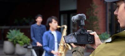 Obrázok kameramana, ktorý natáča hudobníkov v jednosmernom režime s mikrofónom ECM-B10 pripevneným ku kamere.