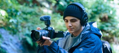 Un caméraman tourne dans la nature, en contrôlant le son avec un casque. L'appareil photo est équipé d'un ECM-B10 réglé en mode omnidirectionnel.