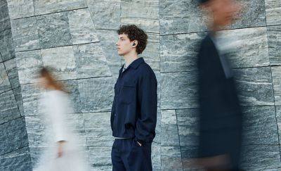 A clear image of a person standing by a wall with people around that are blured
