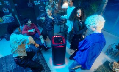 A group of people dancing in a darkened room around the TOWER 9AC speaker with its party lights on