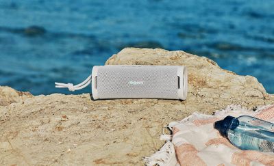 The ULT FIELD 1 portable speaker sitting on a rock at the beach.