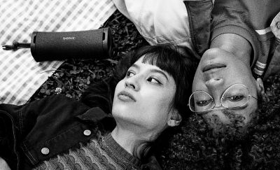 A black and white image of two young people lying down with The FIELD 1 Portable Speaker lying beside them.