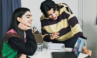 Two people making a video call on a laptop with an ULT FIELD 1 portable speaker providing the audio.