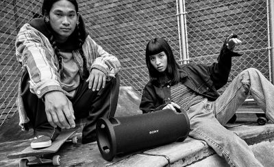 Black and white image of two young people sitting at a skate park with the ULT FIELD 7 portable speaker.