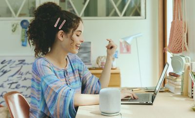 A young woman working at a laptop on a desk with the LinkBuds Speaker in the foreground.