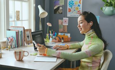 Girl sitting at desk with her laptop and phone listening with ear buds