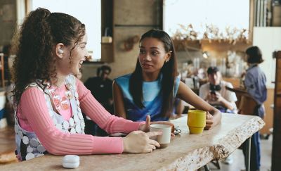 Two friends talking in a cafe, one of whom has a LinkBuds Fit in their ear.