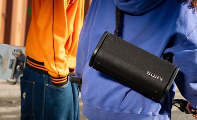 A person with their friend riding their bike  down the street with the ULT FIELD 5 hanging from the should strap across their back