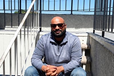 Bald person with beard and sunglasses sitting on concrete steps.
