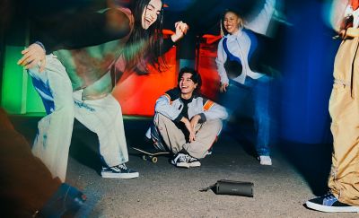 A group of young people dancing around the ULT FIELD 1  Portable Speaker.