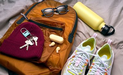 WF-C510 earbuds and respective case in yellow sat on a bed with a backpack and some personal items scattered on the bed