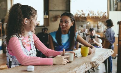 Two friends talking in a cafe, one of whom has a LinkBuds Fit in their ear.