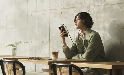 Listener enjoying music with Sony NW‑ZX900 and wired headphones inside a bright café