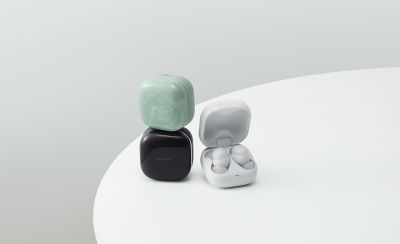 A green LinkBuds Fit case stacked on top of a black one, with a white case beside it opened to reveal the LinkBuds Fit earbuds inside.