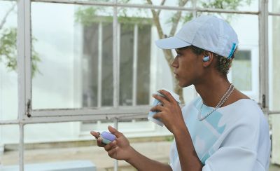 A young man in a white baseball cap and a white jumper wearing a pair of LinkBuds Fit earbuds.