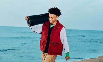 A young person walking along a beach with the ULT FIELD 7 portable speaker on their shoulder.