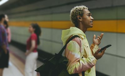 A young man talking on the phone through his LinkBuds Fit while stood on the platform in a train station.