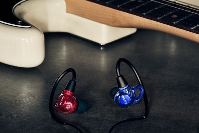 Audífonos Sony rojos y azules colocados sobre una superficie oscura junto a una guitarra